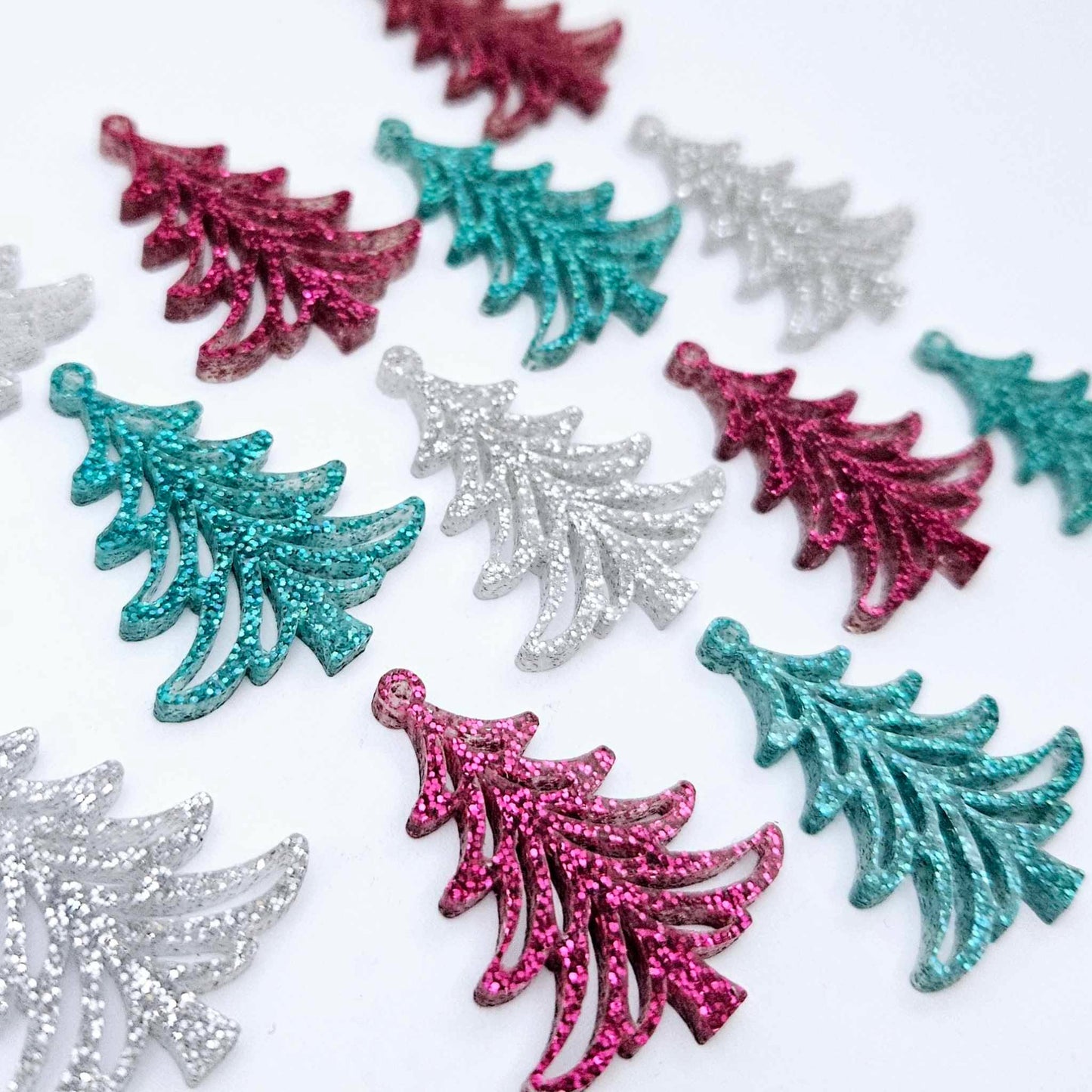 A mixture of hot pink glitter, teal glitter and silver glitter 35mm Cascade Christmas Tree dangle blanks laying flat on a white background