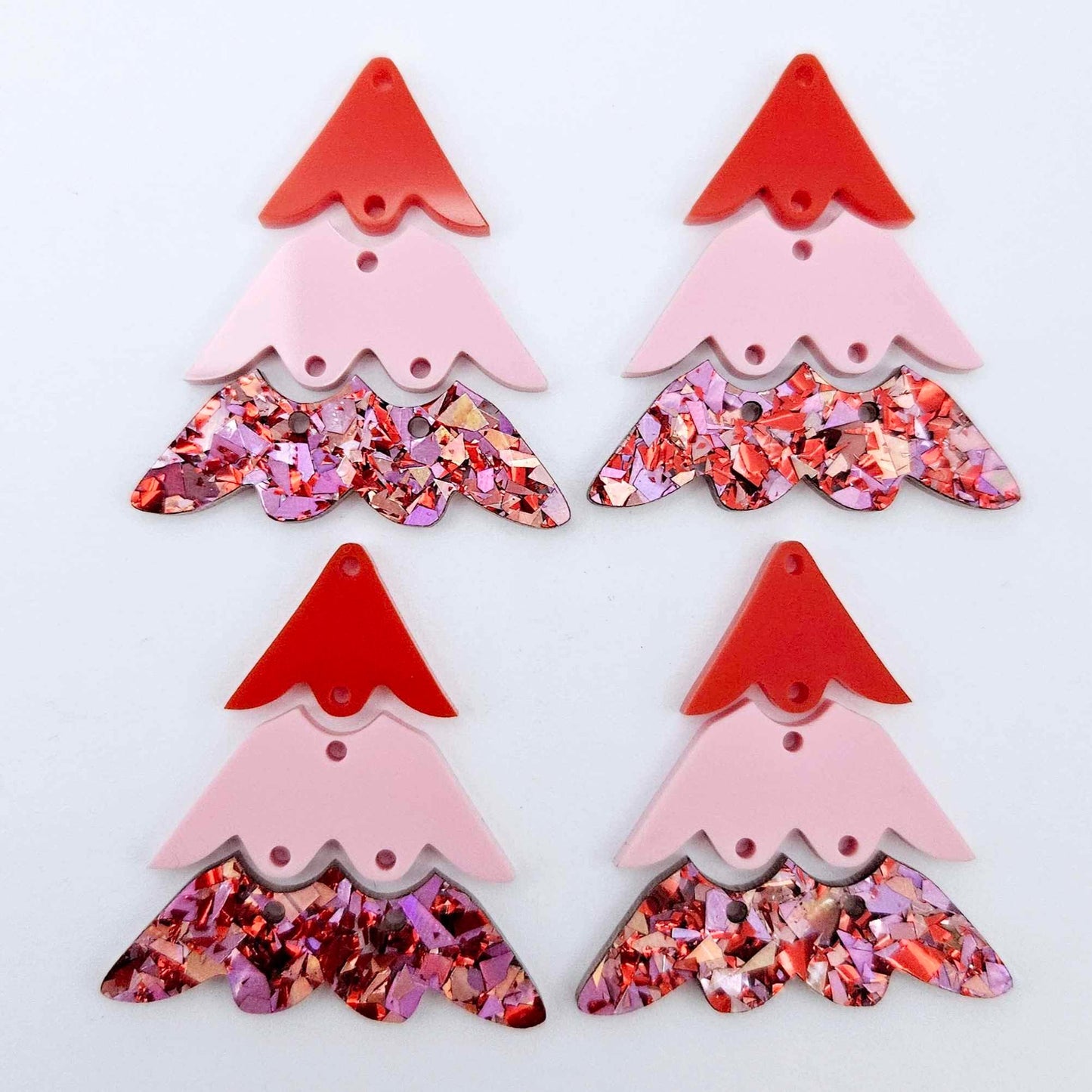 Two pairs of 40mm three piece Christmas Tree dangle earring blanks in Chunky Love Glitter, Pastel Pink and Solid Red acrylic laying flat on a white background