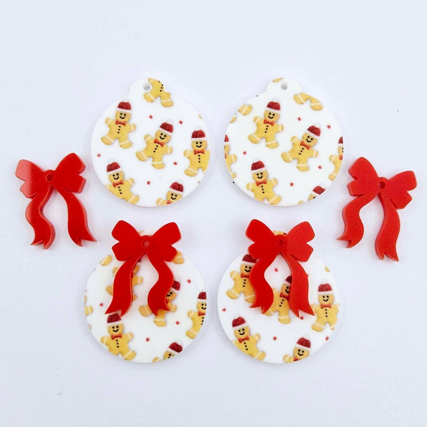 Two pairs of Gingerbread Party UV printed bauble dangle blanks with included red bows laying flat