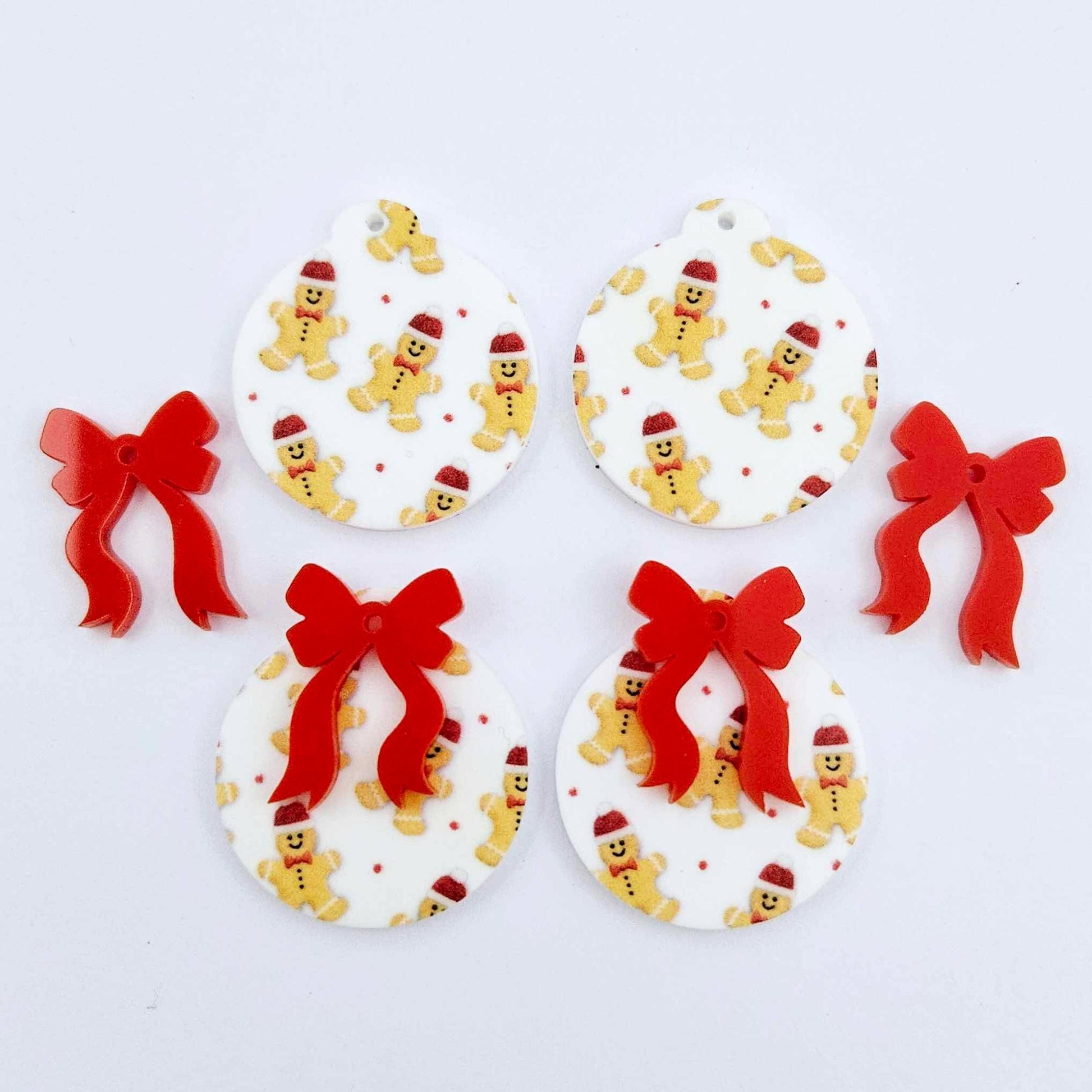 Two pairs of Gingerbread Party UV printed bauble dangle blanks with included red bows laying flat