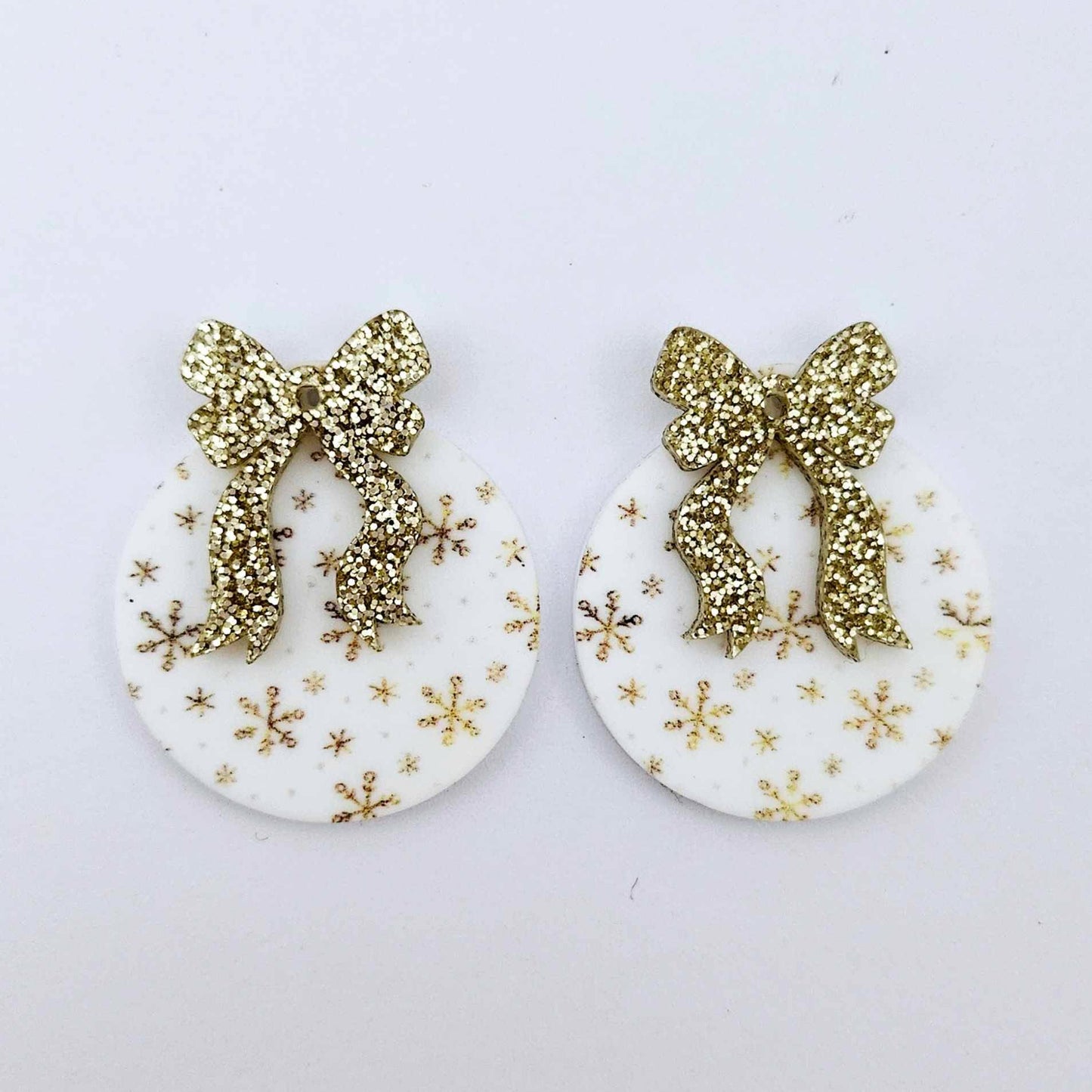 One pair of white Christmas Snowflake UV printed bauble dangle blanks with gold glitter bow connectors laying flat