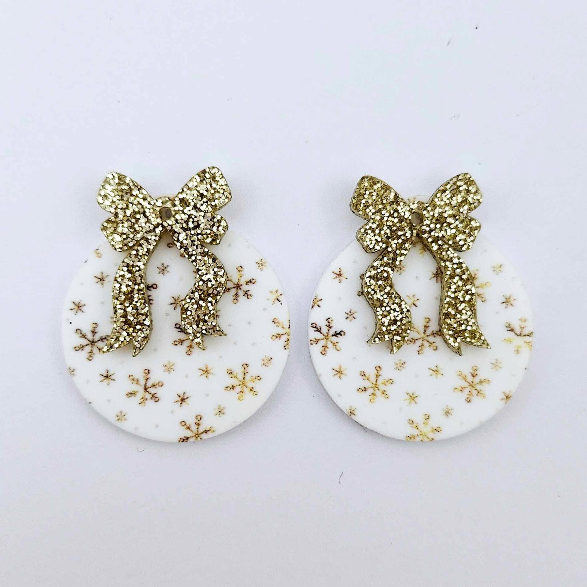 One pair of white Christmas Snowflake UV printed bauble dangle blanks with gold glitter bow connectors laying flat