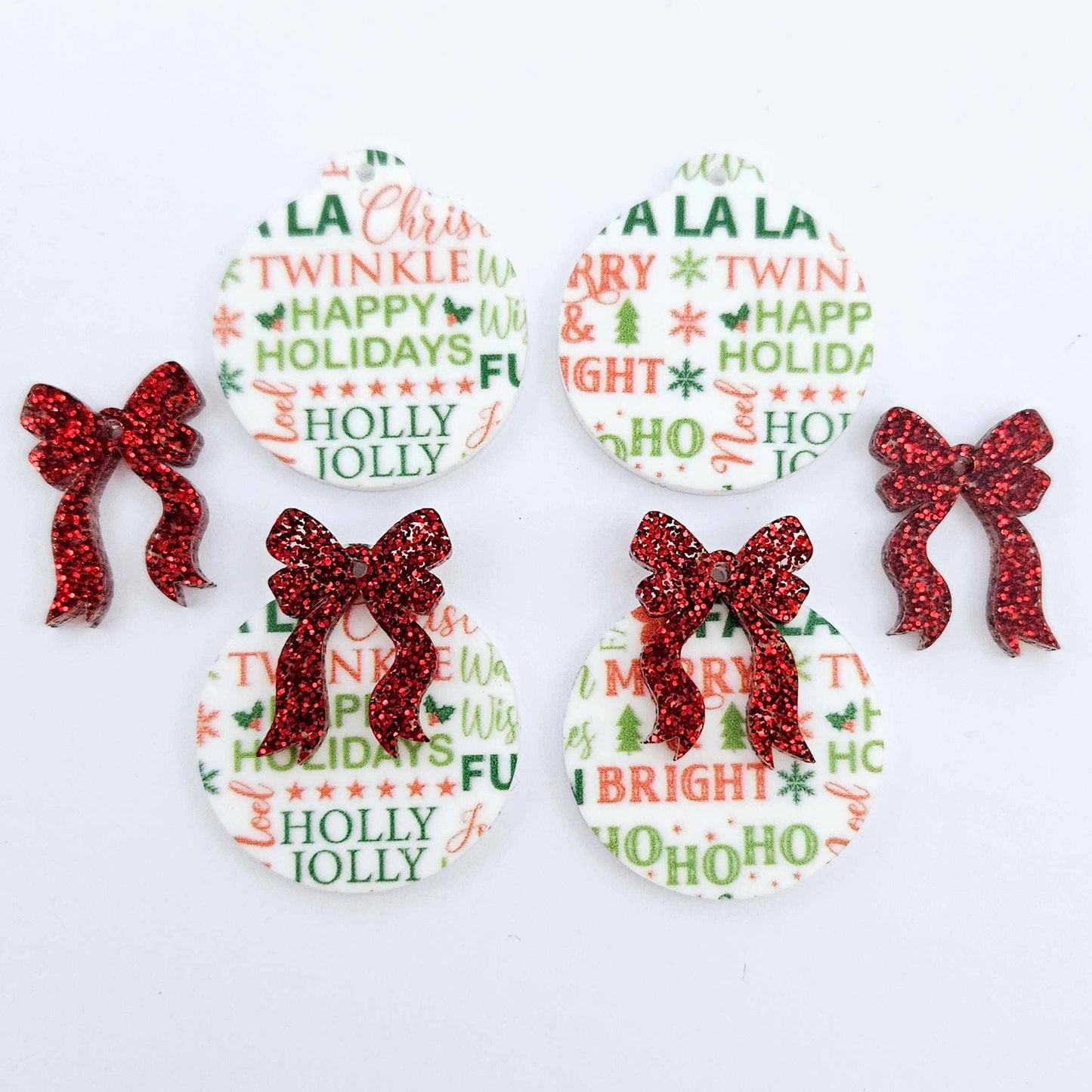 Two pairs of Christmas Text UV printed bauble dangle blanks with included red glitter bows laying flat