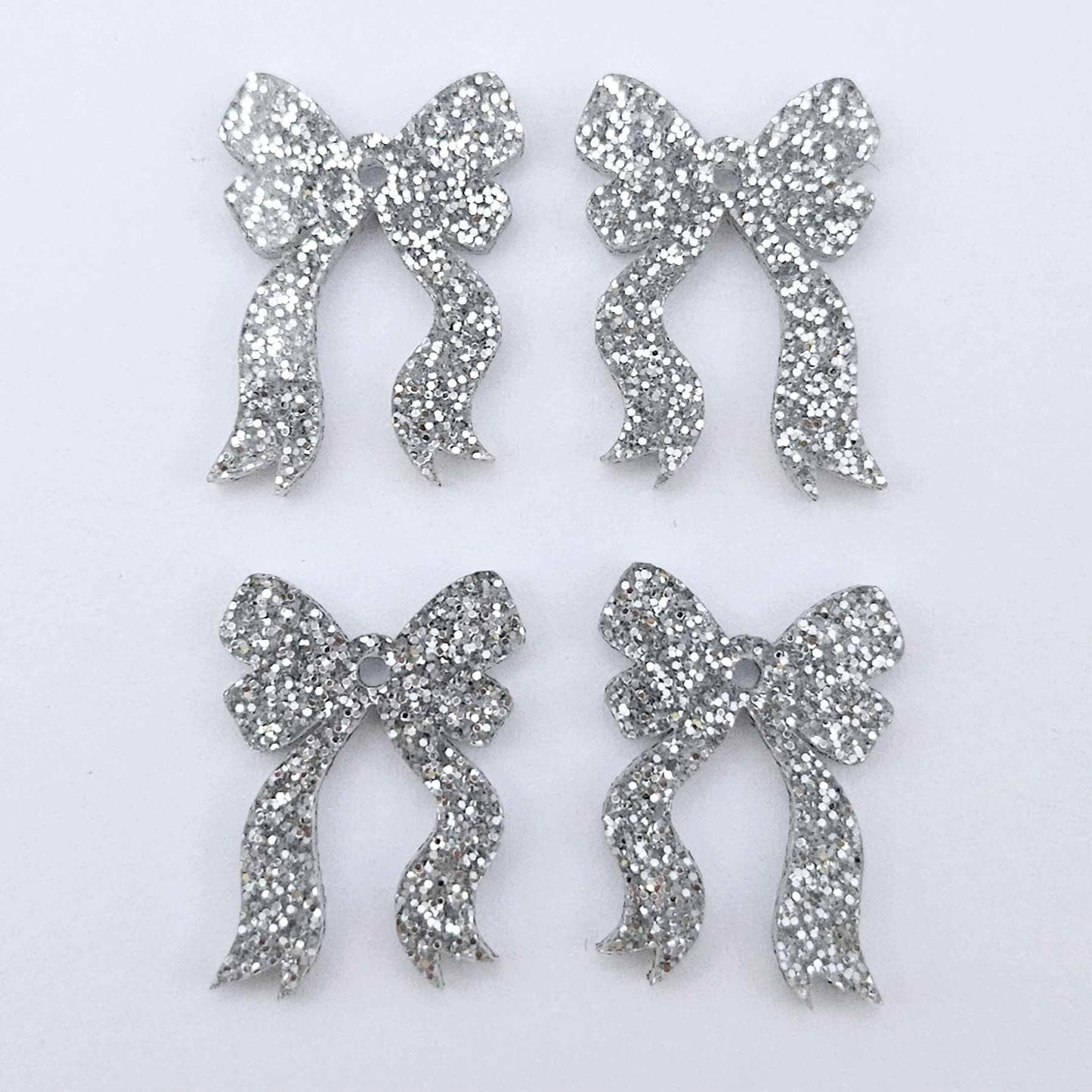Two pairs of silver glitter acrylic bow dangle earring blanks laying flat