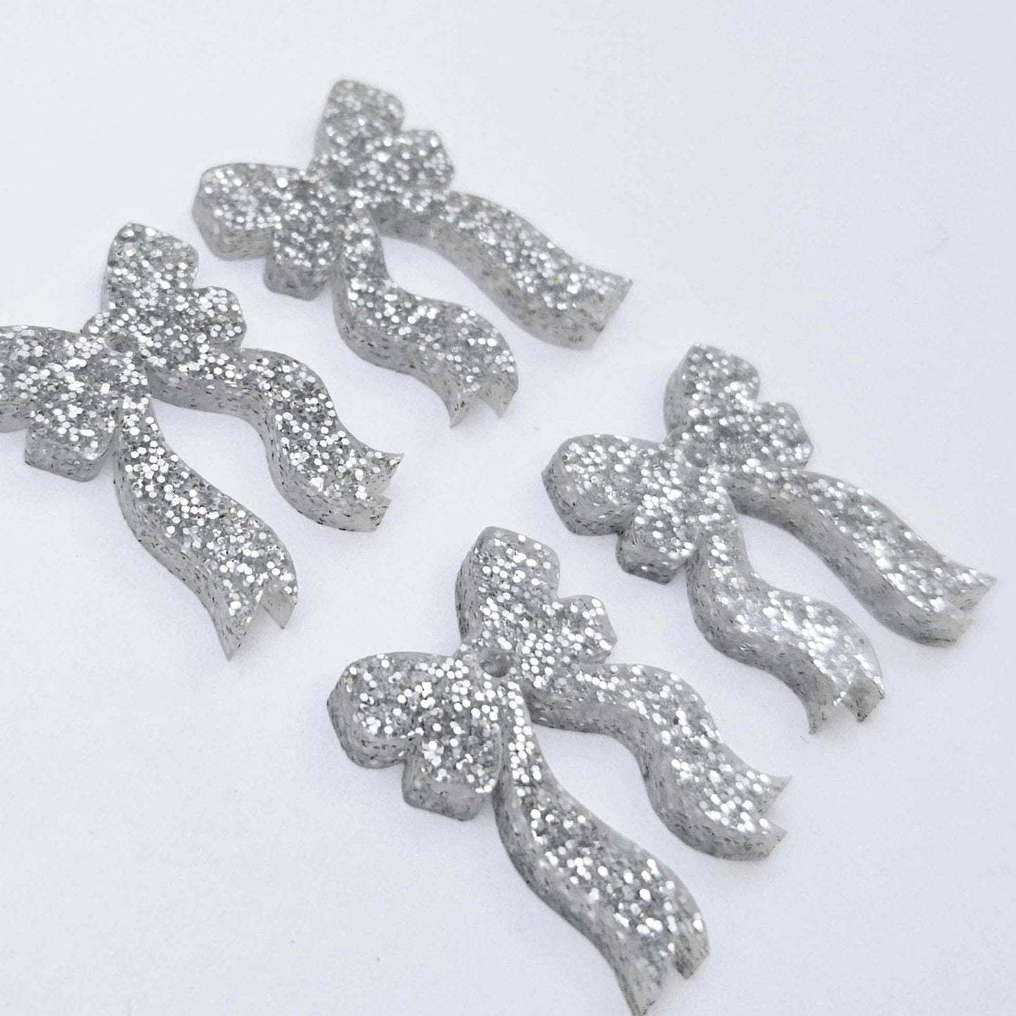 Two pairs of silver glitter acrylic bow dangle earring blanks laying flat