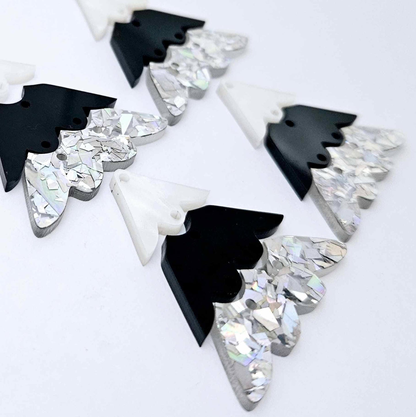 Two pairs of 40mm three piece Christmas Tree dangle earring blanks in holographic silver glitter, black and white marble acrylic laying flat on a white background
