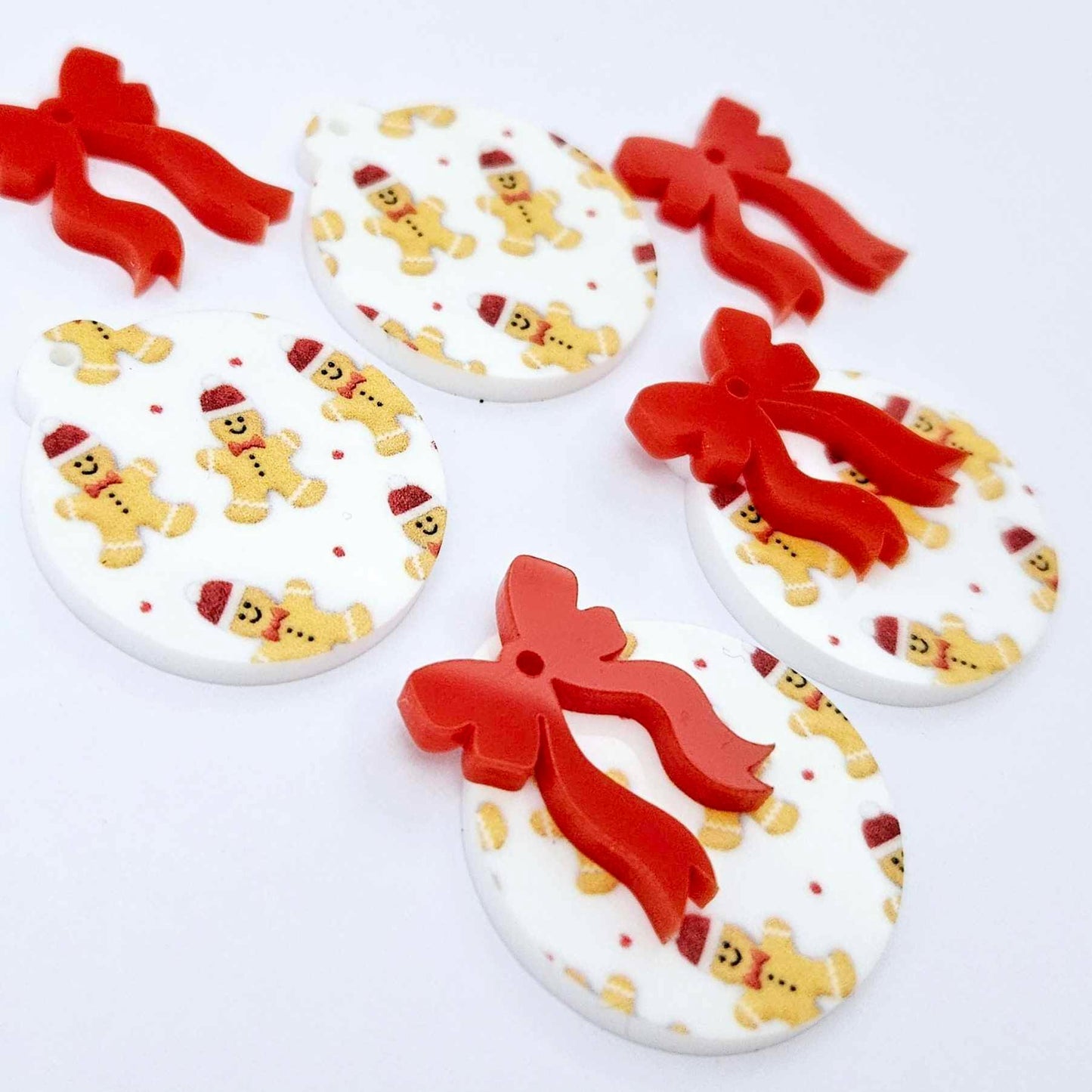 Two pairs of Gingerbread Party UV printed bauble dangle blanks with included red bows laying flat