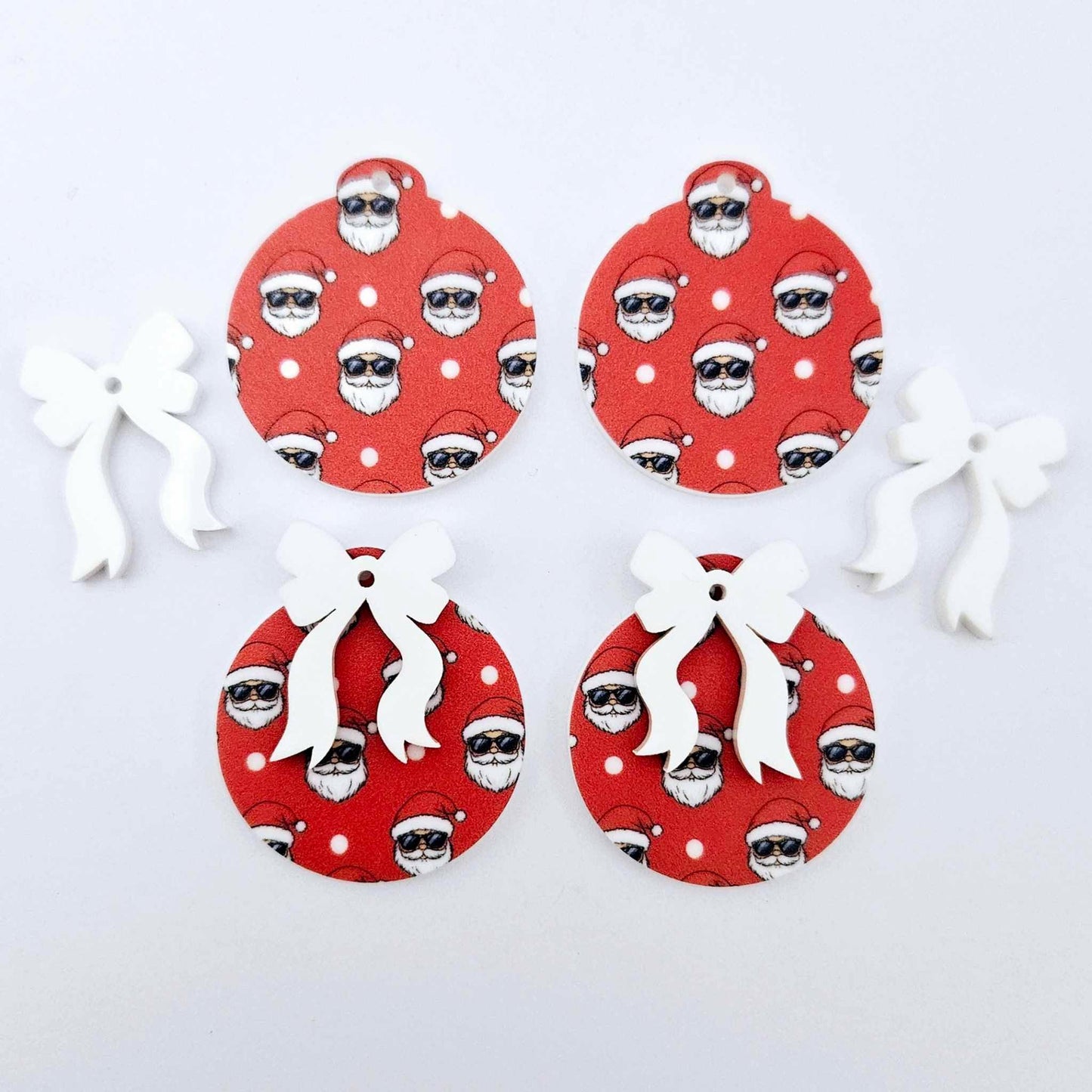 Two pairs of Jolly Cool UV printed bauble dangle blanks with included white bows laying flat