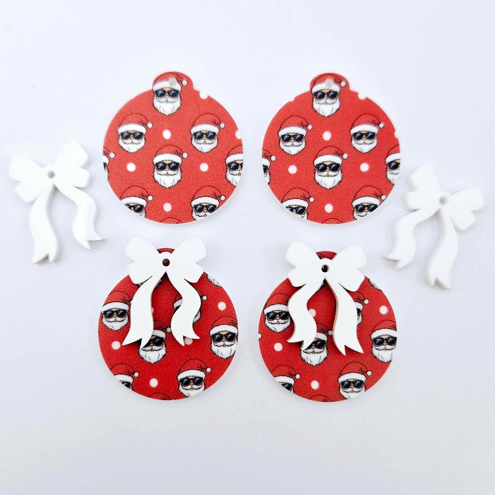 Two pairs of Jolly Cool UV printed bauble dangle blanks with included white bows laying flat