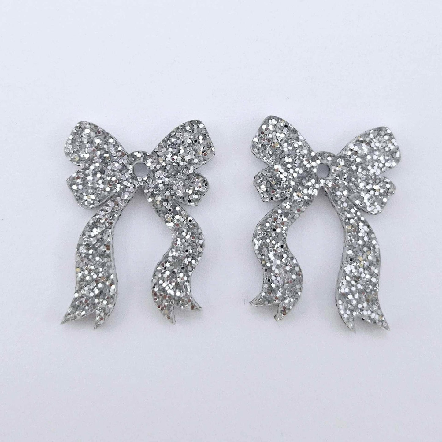 One pair of silver glitter acrylic bow dangle earring blanks laying flat