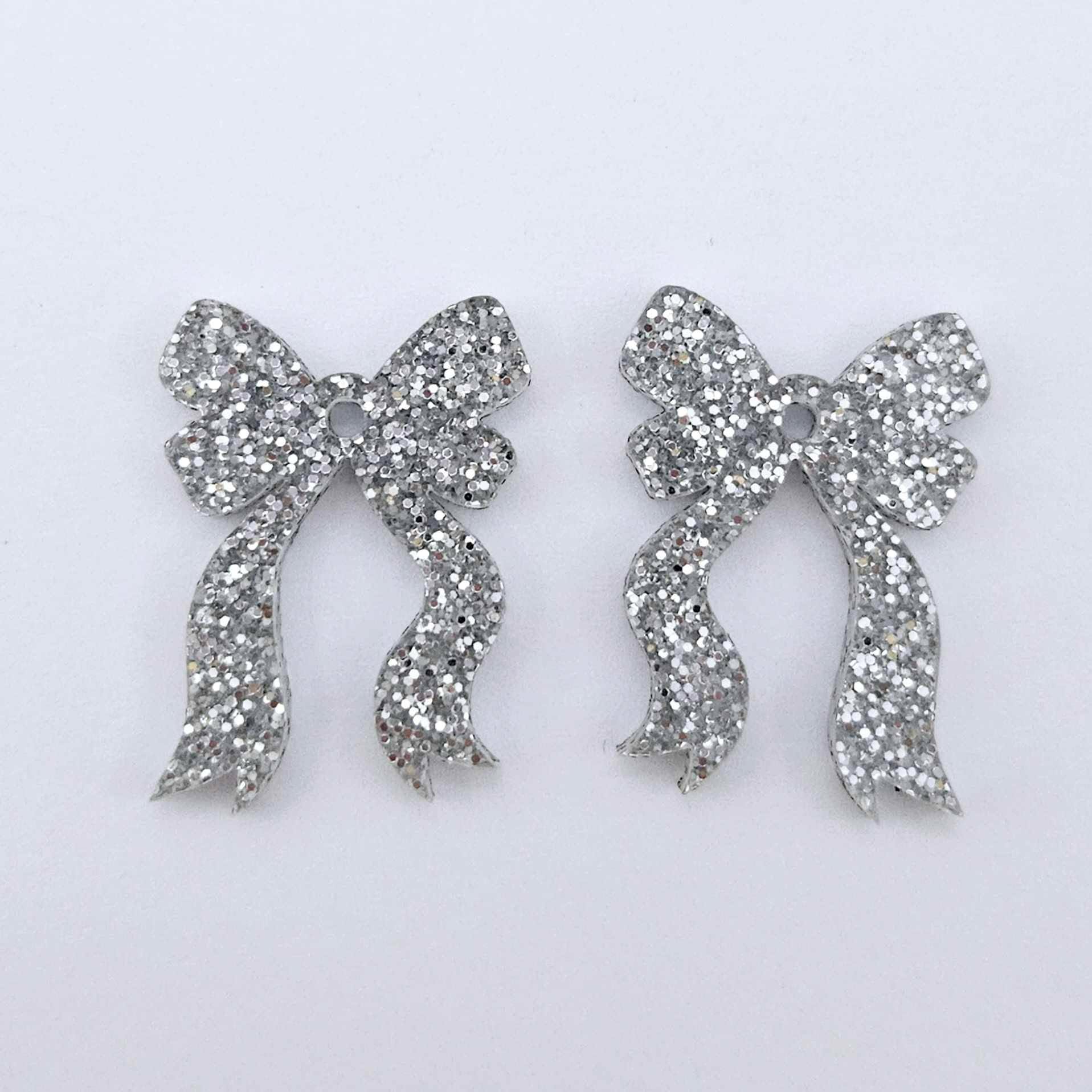 One pair of silver glitter acrylic bow dangle earring blanks laying flat