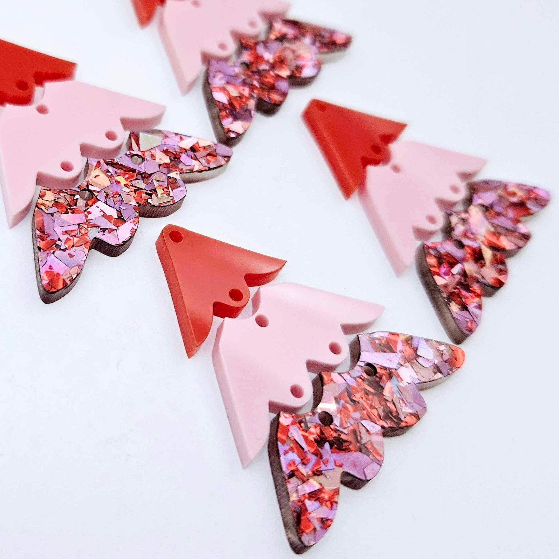 Two pairs of 40mm three piece Christmas Tree dangle earring blanks in Chunky Love Glitter, Pastel Pink and Solid Red acrylic laying flat on a white background