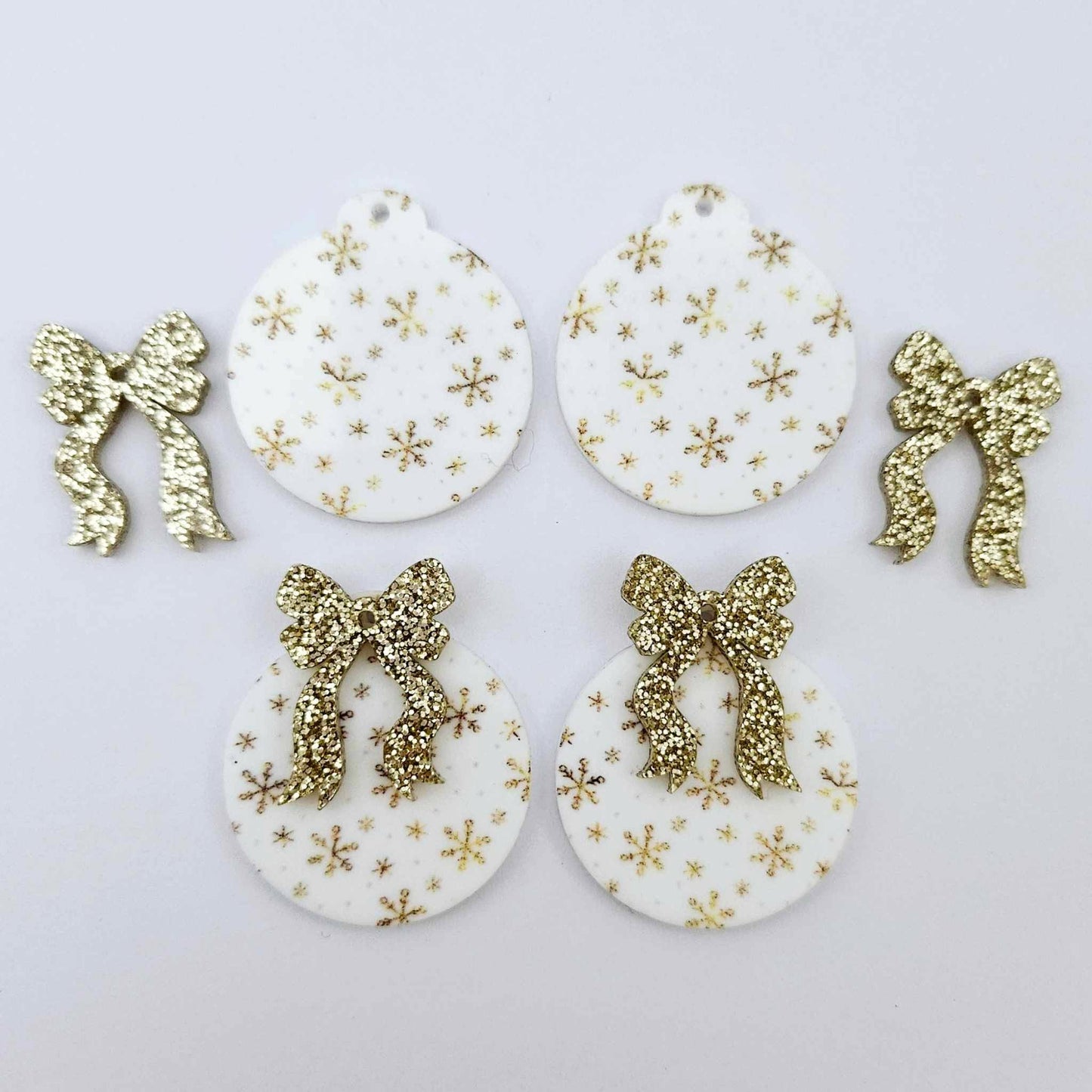 Two pairs of white Christmas Snowflake UV printed bauble dangle blanks with gold glitter bow connectors laying flat