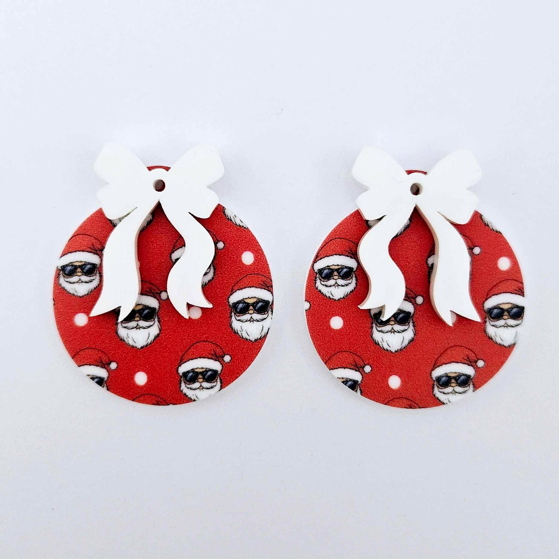 One pair of Jolly Cool UV printed bauble dangle blanks with included white bows laying flat