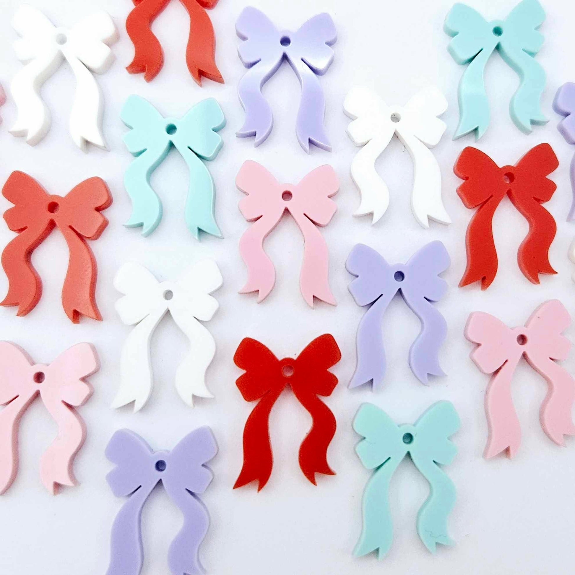 A selection of solid red, white, pastel pink, pastel purple and pastel aqua acrylic bow dangle earring blanks laying flat