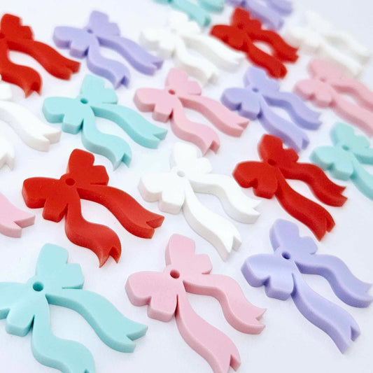 A selection of solid red, white, pastel pink, pastel purple and pastel aqua acrylic bow dangle earring blanks laying flat