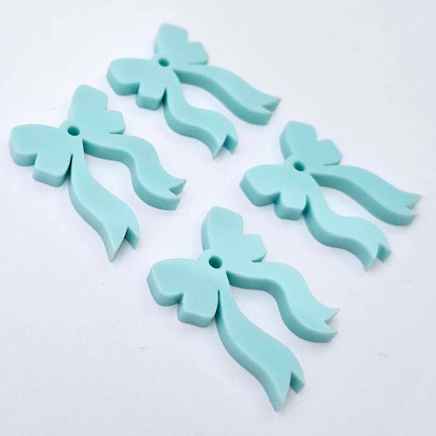 Two pairs of pastel aqua acrylic bow dangle earring blanks laying flat