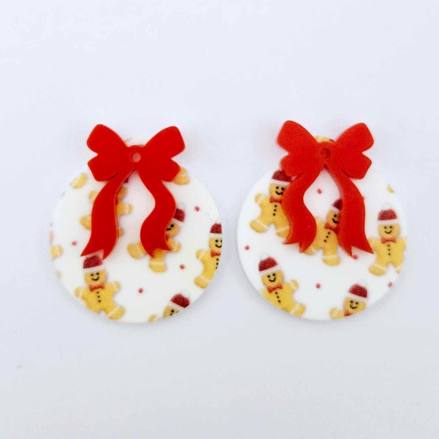 One pair of Gingerbread Party UV printed bauble dangle blanks with included red bows laying flat