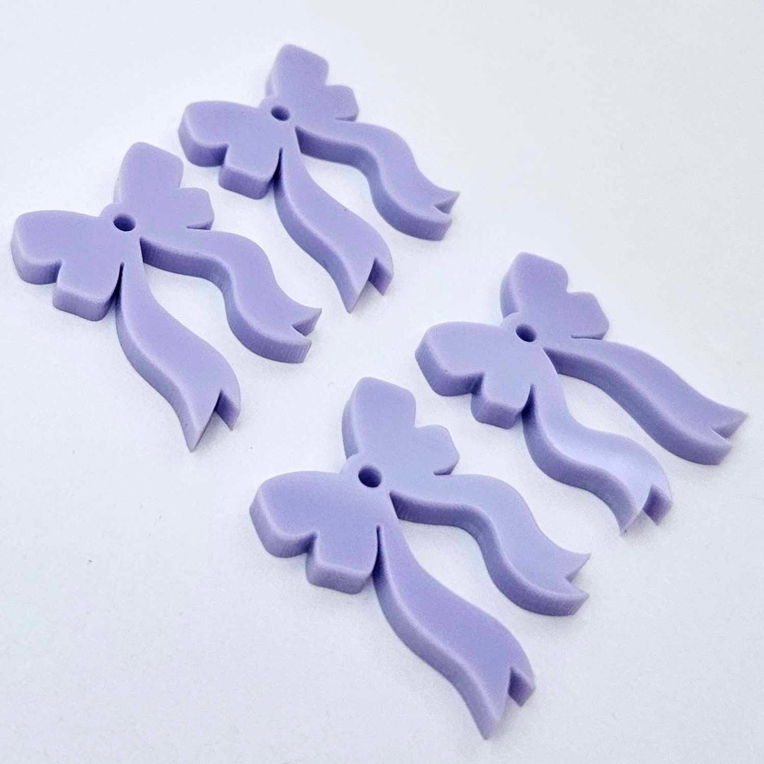 Two pairs of pastel purple acrylic bow dangle earring blanks laying flat