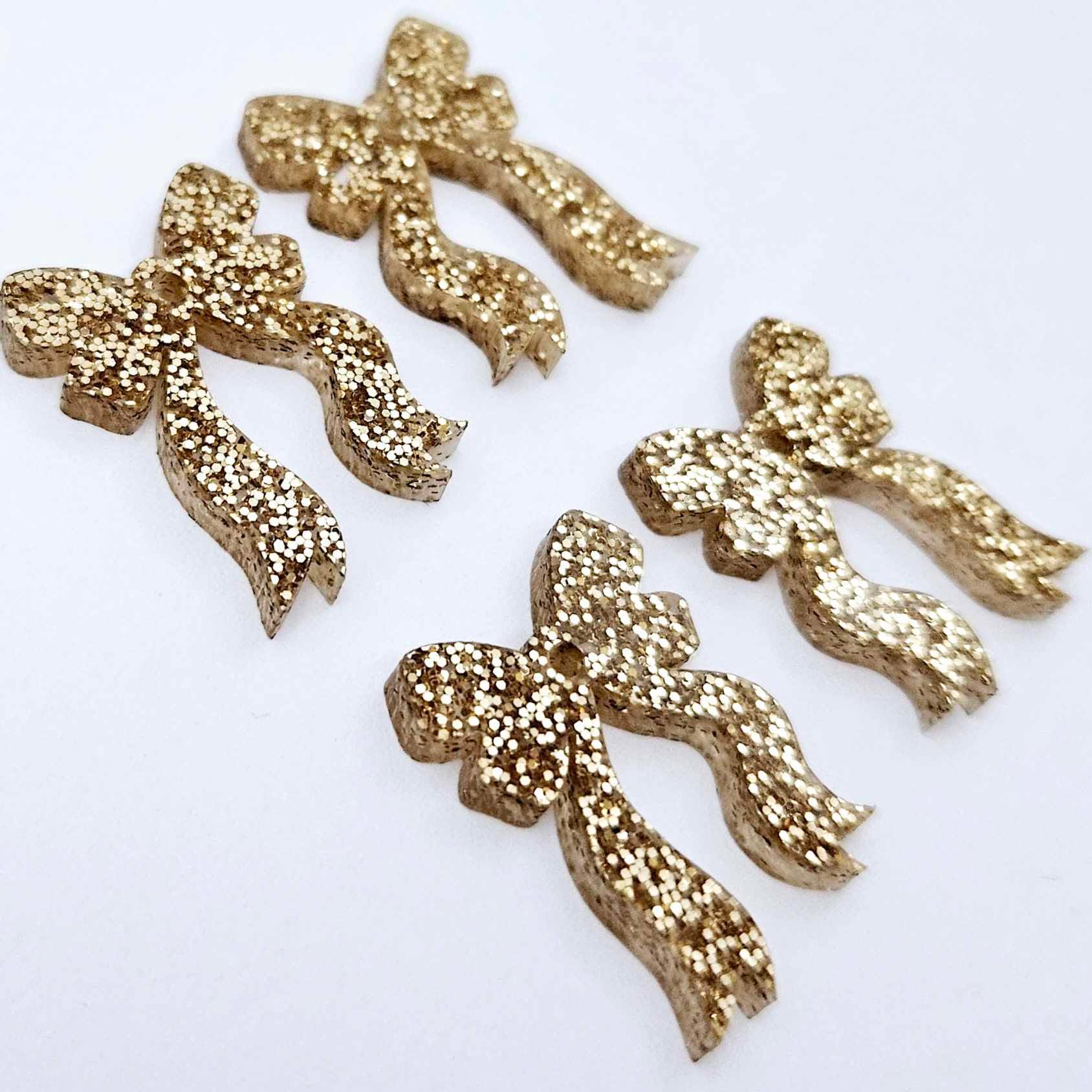 Two pairs of rose gold glitter bow dangle earring blanks laying flat