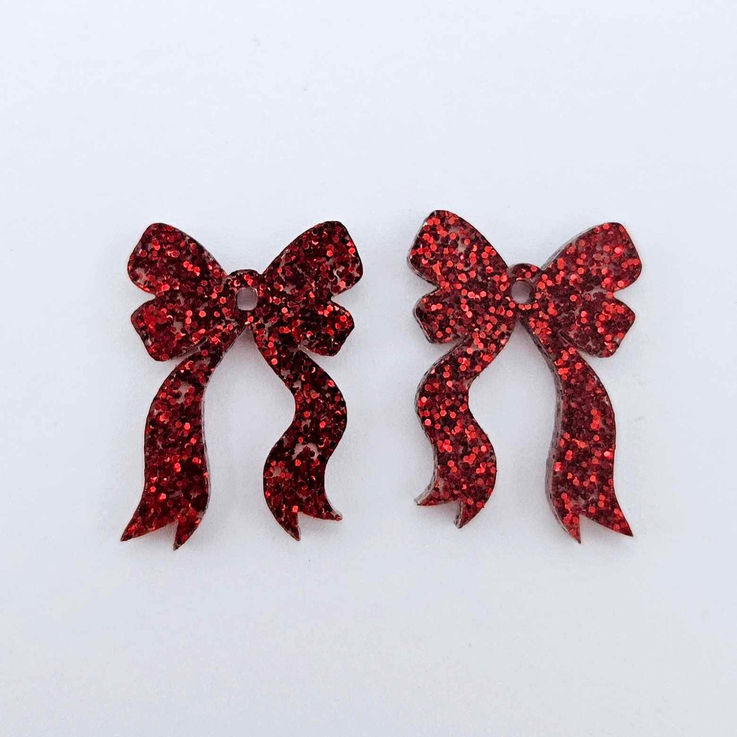 One pair of red glitter acrylic bow dangle earring blanks laying flat