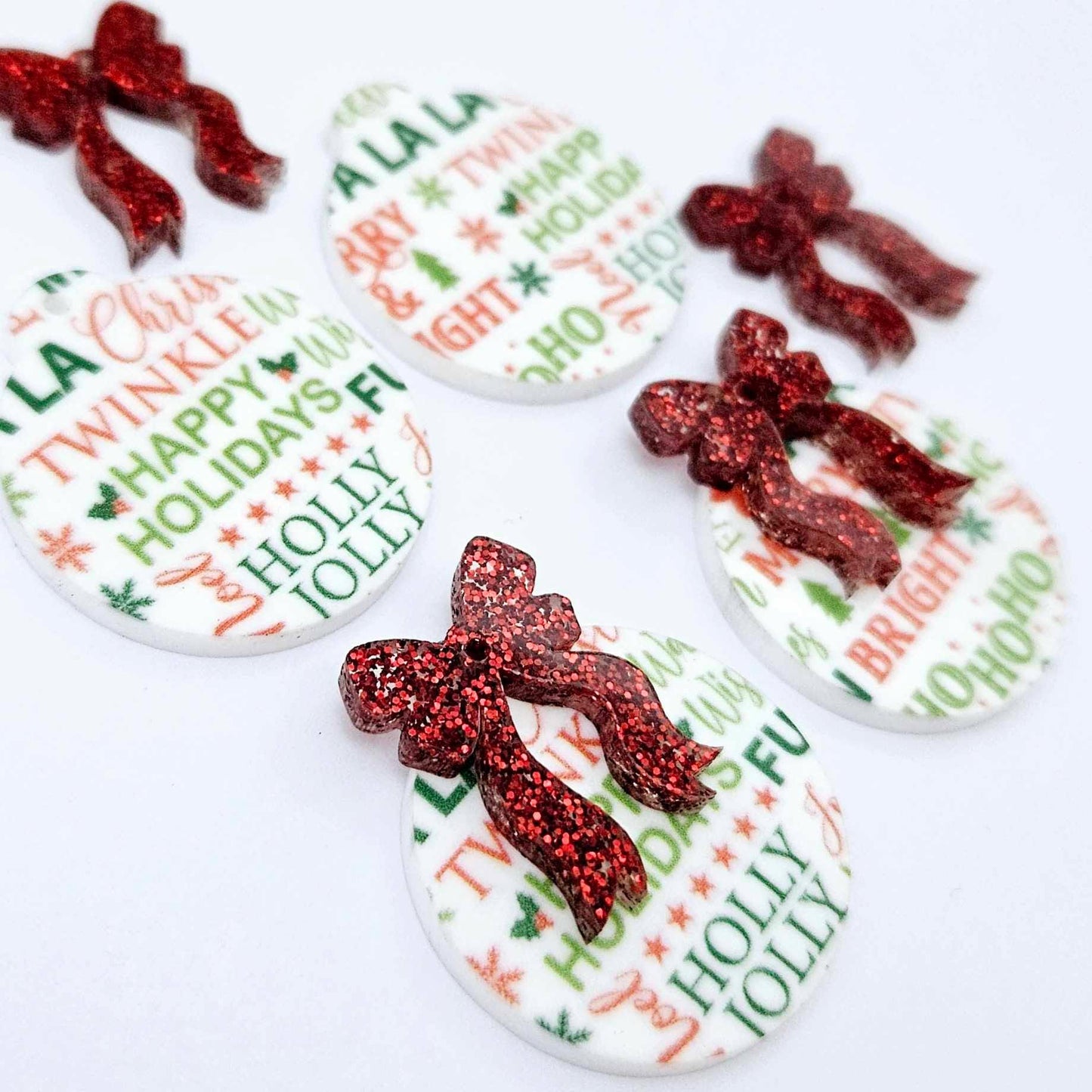 Two pairs of Christmas Text UV printed bauble dangle blanks with included red glitter bows laying flat