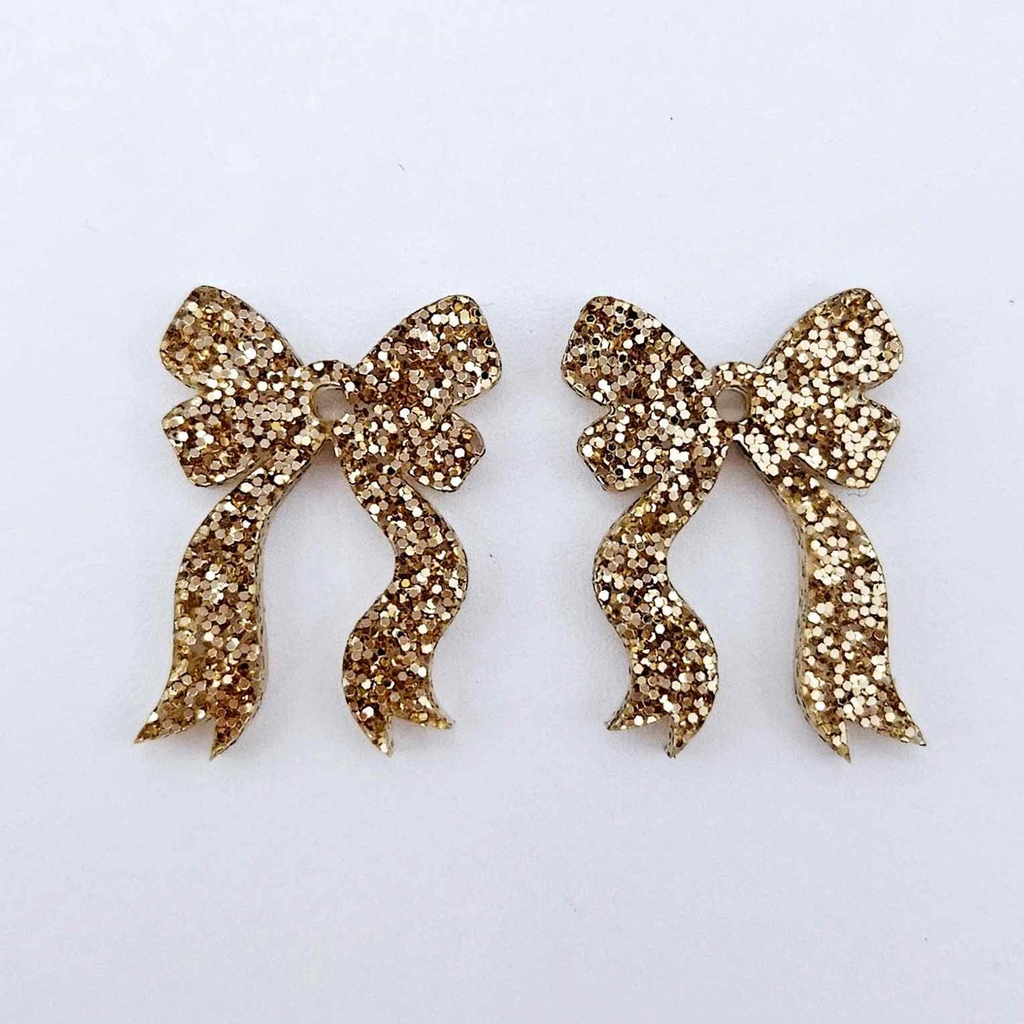One pair of rose gold glitter bow dangle earring blanks laying flat