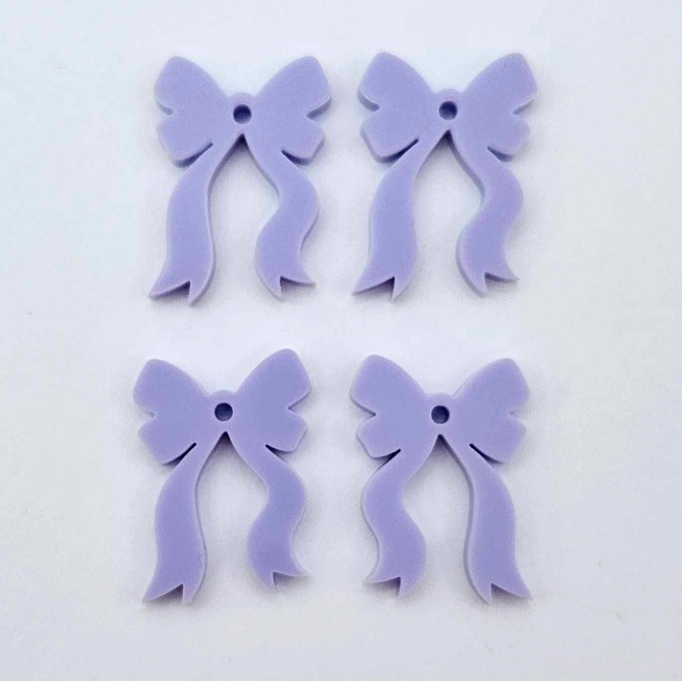 Two pairs of pastel purple acrylic bow dangle earring blanks laying flat