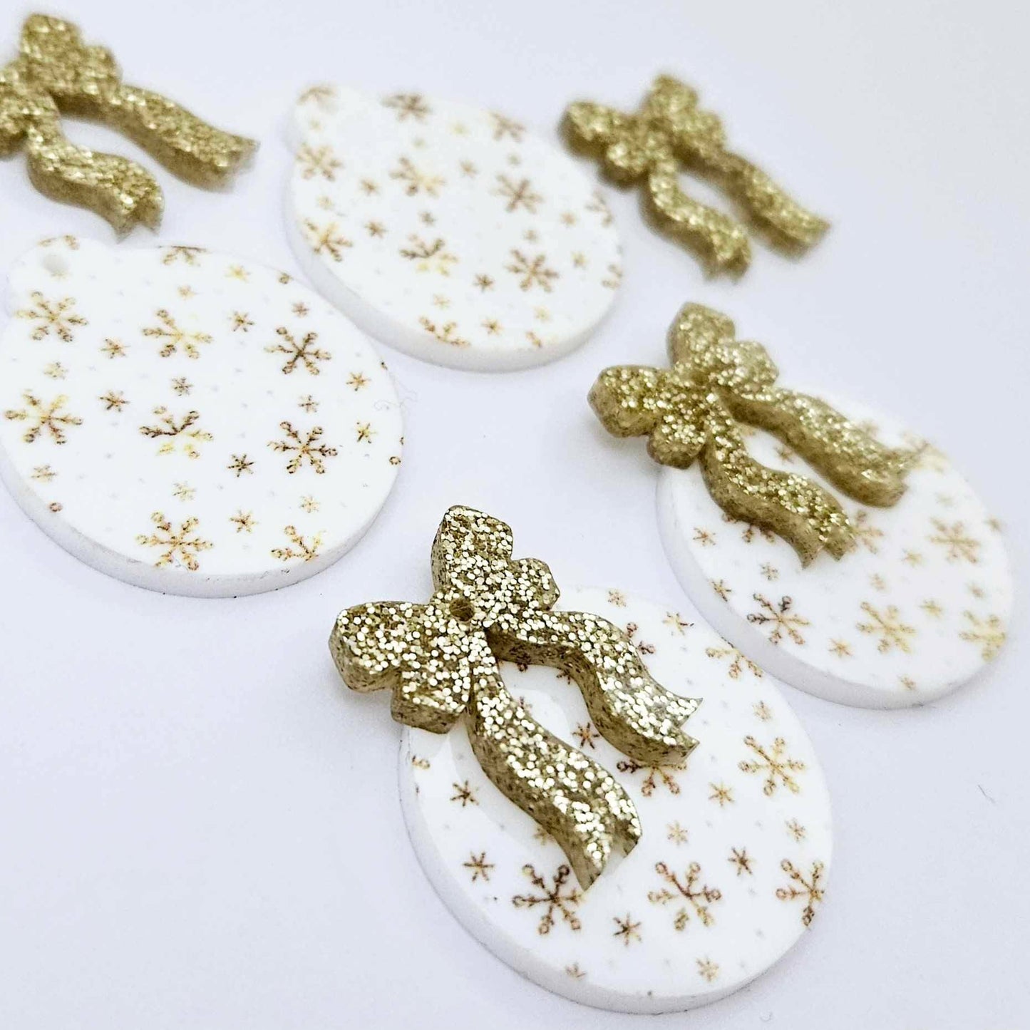 Two pairs of white Christmas Snowflake UV printed bauble dangle blanks with gold glitter bow connectors laying flat