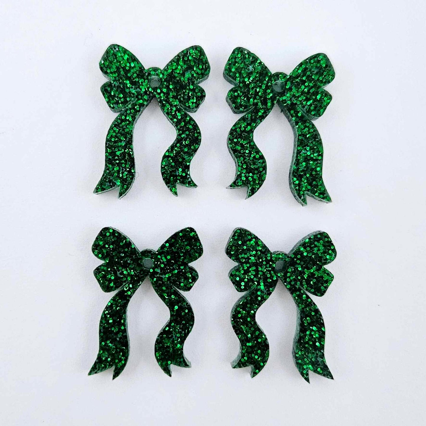 Two pairs of green glitter acrylic bow dangle earring blanks laying flat
