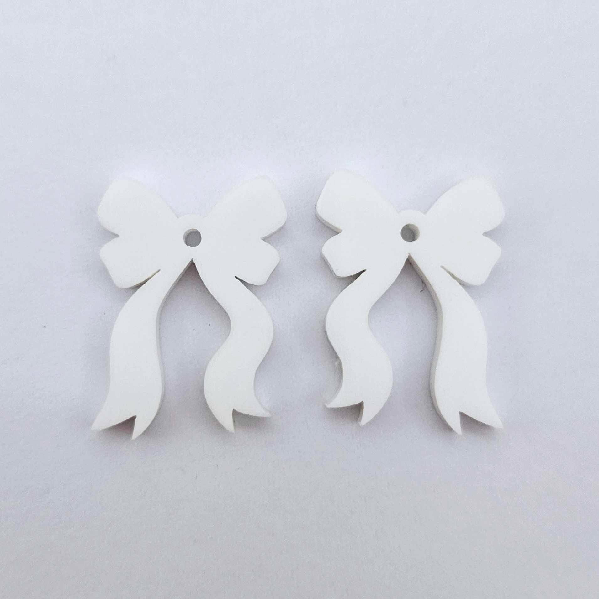 One pair of white acrylic bow dangle earring blanks laying flat