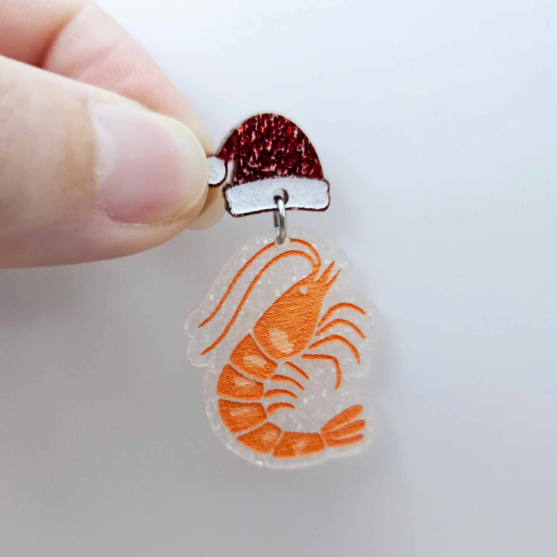 One fairy dust glitter acrylic prawn dangle earring blank assembled with a Santa Hat Topper, shown as a festive Australian Christmas earring
