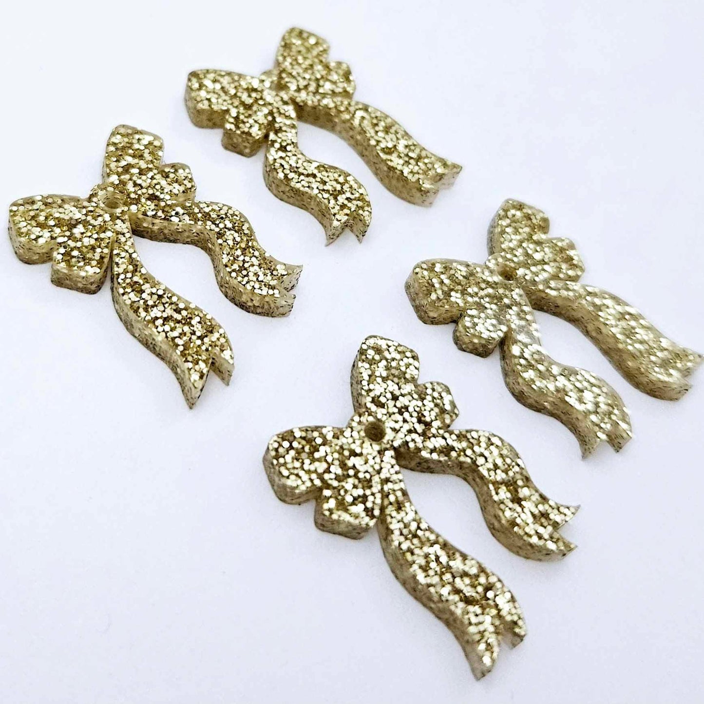 Two pairs of gold glitter acrylic bow dangle earring blanks laying flat