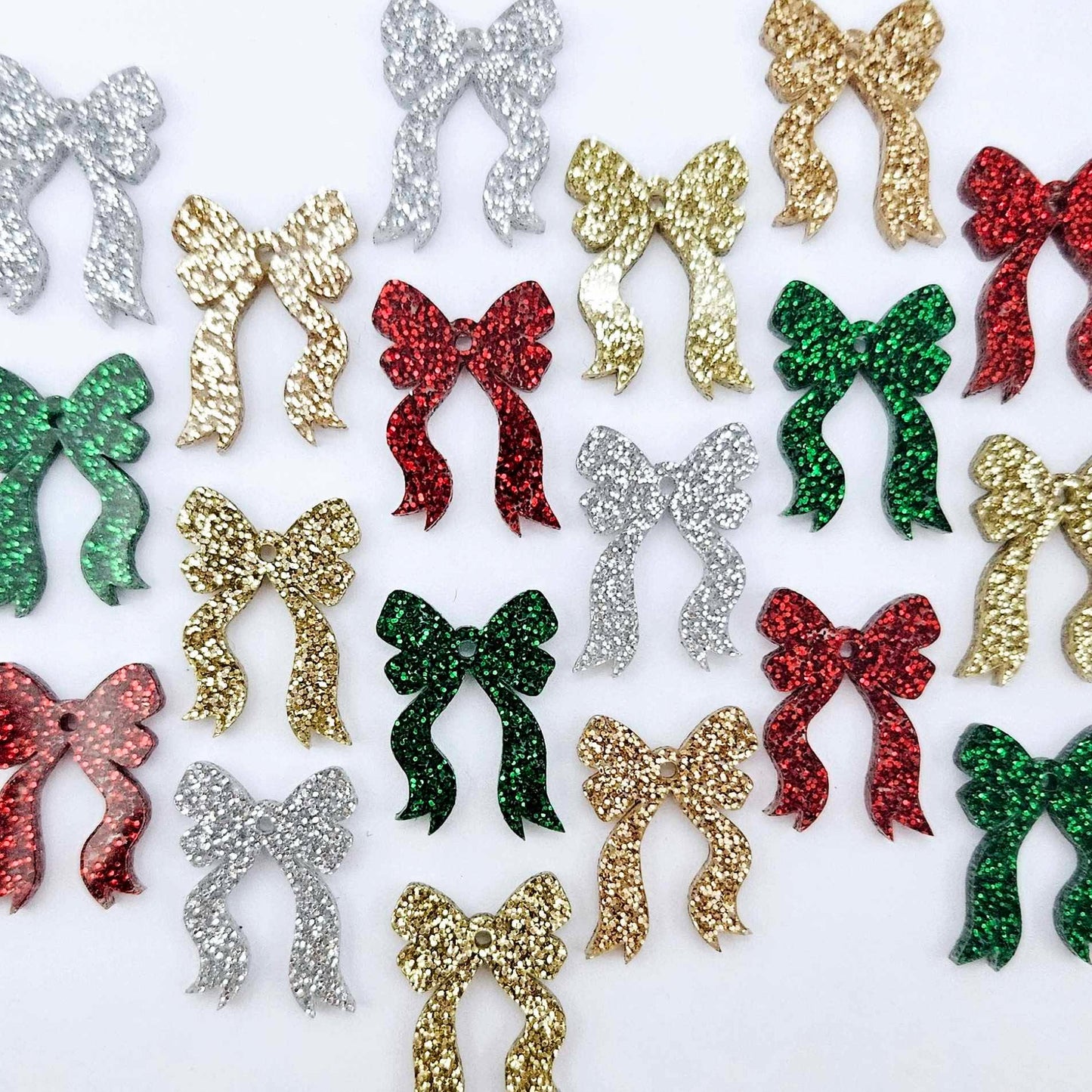 A selection of the traditional glitter acrylic bow dangle earring blanks in red, green, gold, silver and rose gold glitter laying flat