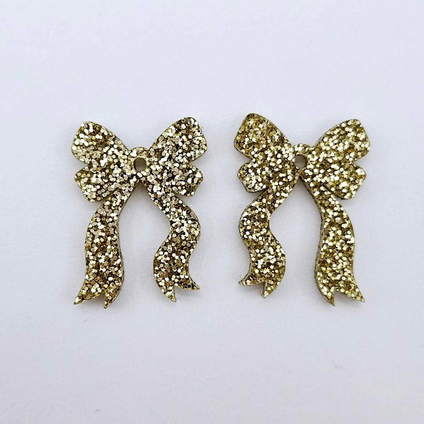One pair of gold glitter acrylic bow dangle earring blanks laying flat