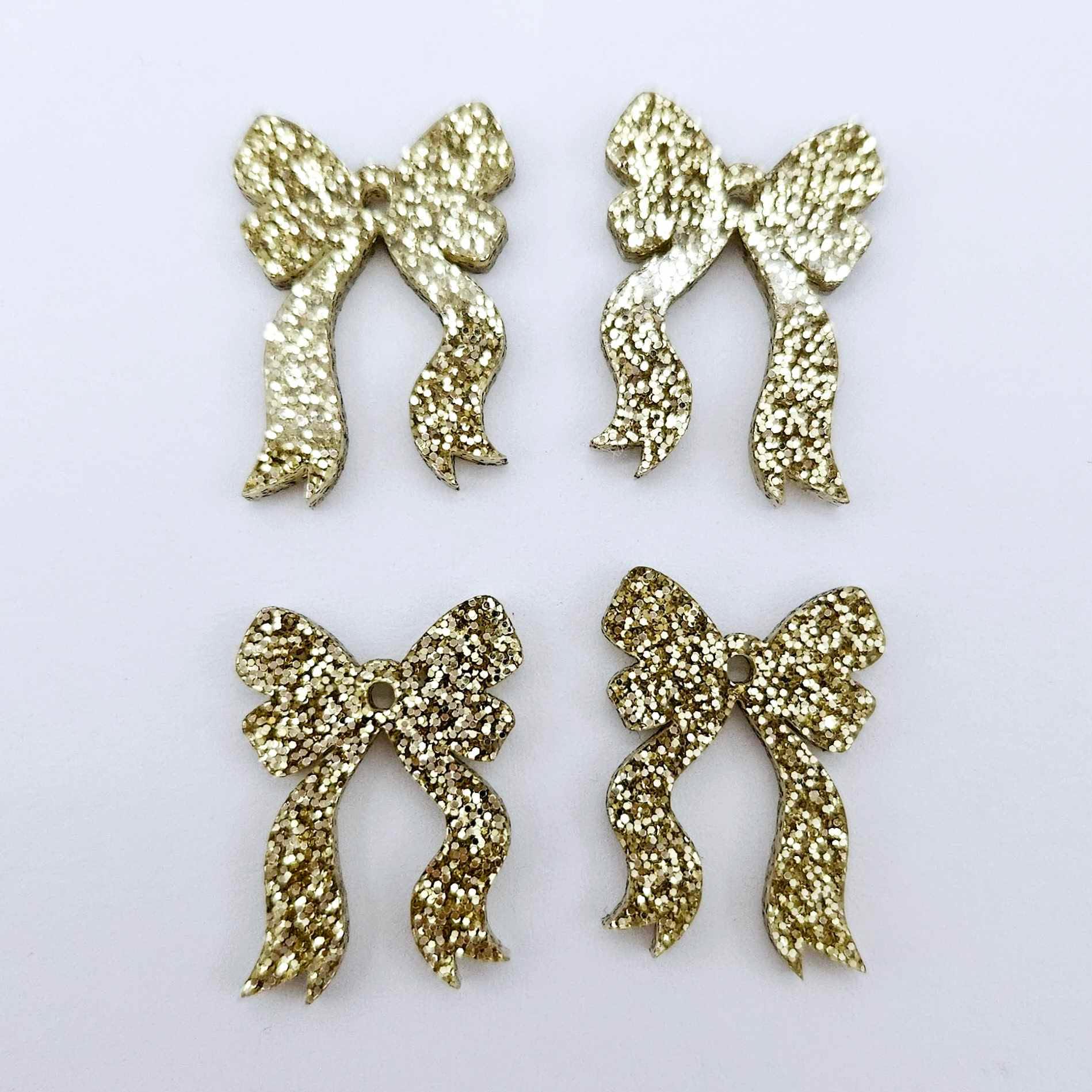 Two pairs of gold glitter acrylic bow dangle earring blanks laying flat