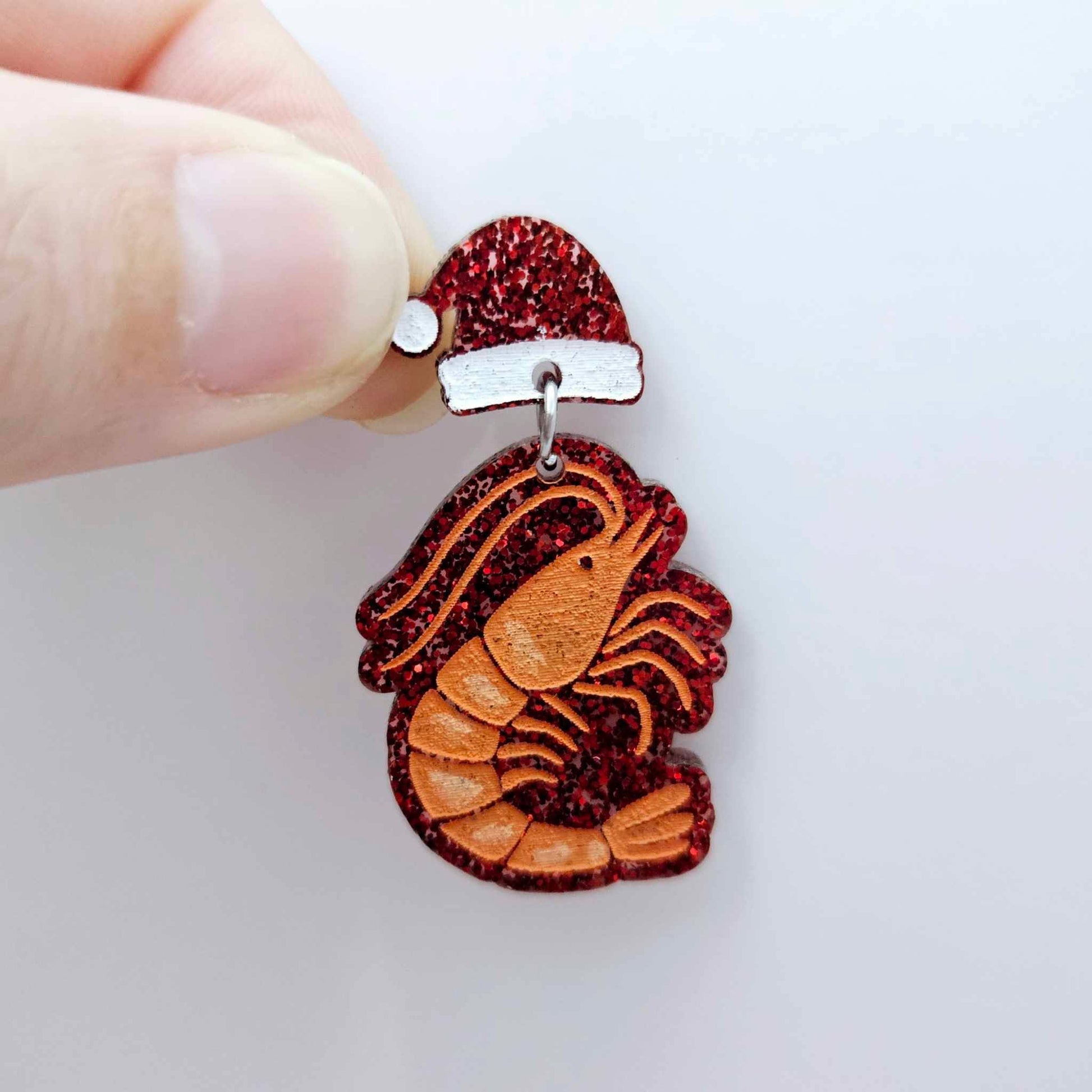 One red glitter acrylic prawn dangle earring blank assembled with a Santa Hat Topper, shown as a festive Australian Christmas earring