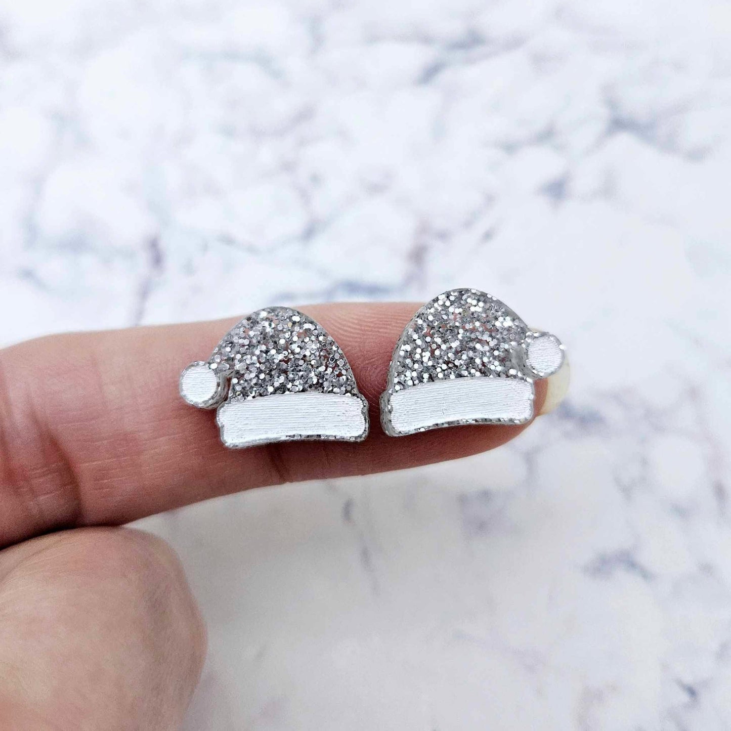 One pair of paint-filled silver glitter acrylic Santa hat stud blanks (no hole) shown on a finger for size reference