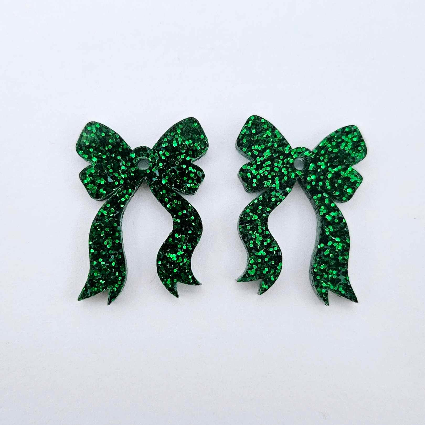 One pair of green glitter acrylic bow dangle earring blanks laying flat