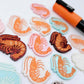 A mixture of Pastel Pink, Pastel Aqua, Red Glitter, Fairy Dust Glitter and White Marble acrylic prawn dangle earring blanks laying flat with an orange posca paint pen