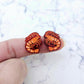 One pair of paint-filled red glitter acrylic prawn stud earring blanks shown on a finger for size reference