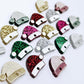 A selection of paint-filled glitter crylic Santa hat toppers in red, green, gold, silver and hot pink, with multiple unpainted pieces still covered with protective paper