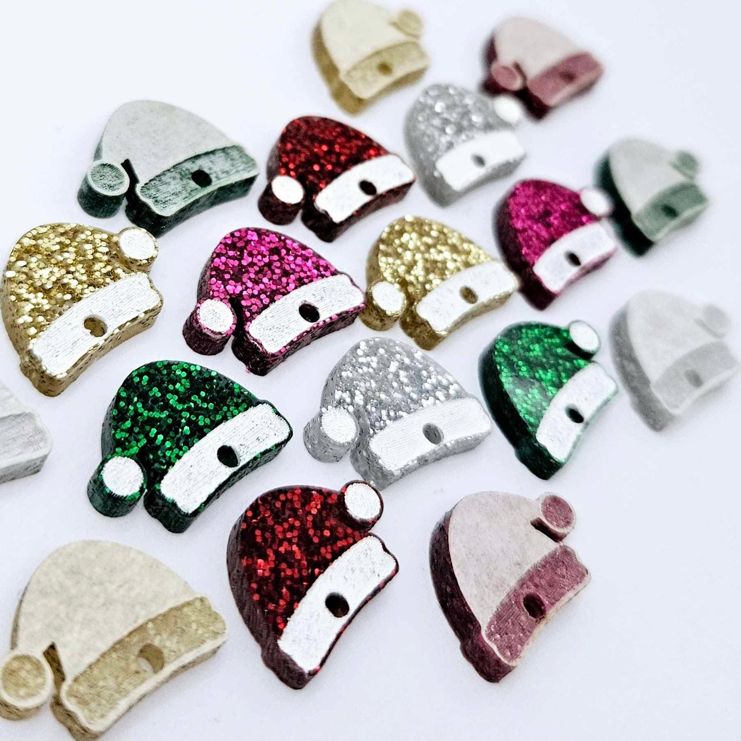 A selection of paint-filled glitter crylic Santa hat toppers in red, green, gold, silver and hot pink, with multiple unpainted pieces still covered with protective paper