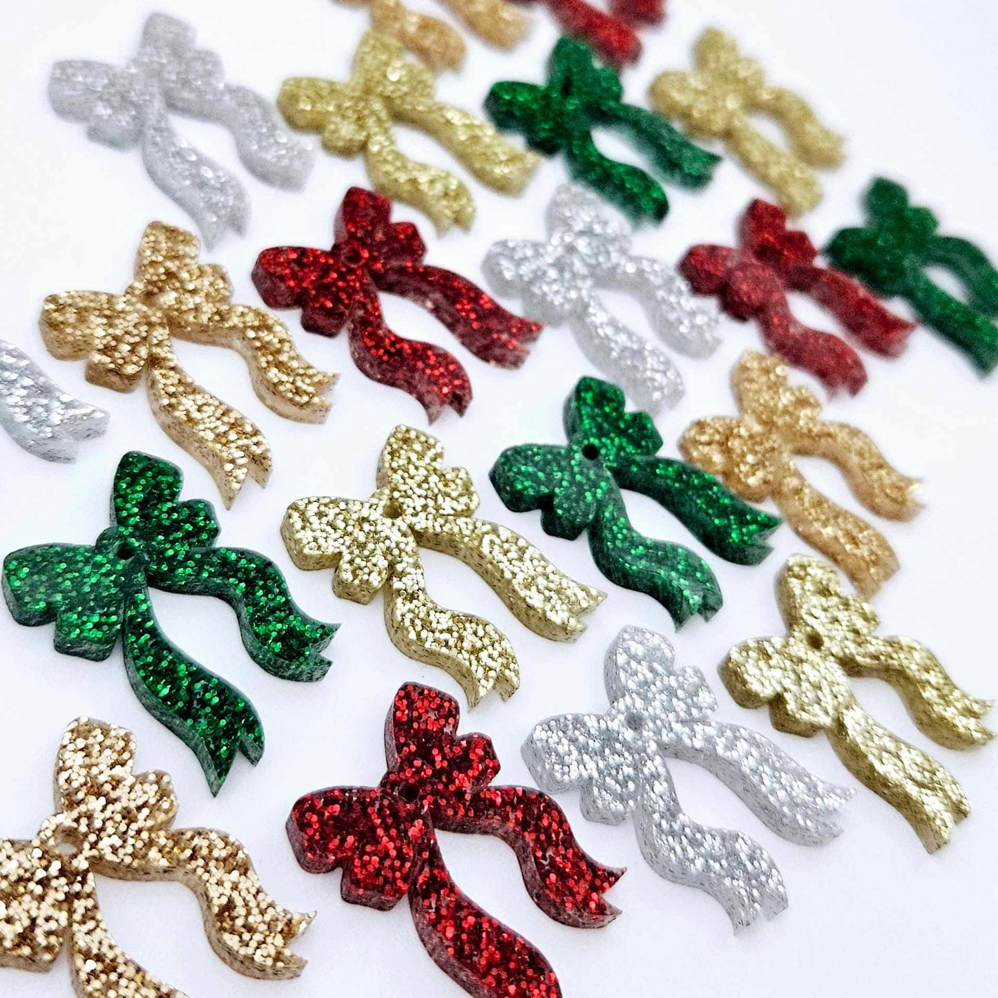 A selection of the traditional glitter acrylic bow dangle earring blanks in red, green, gold, silver and rose gold glitter laying flat