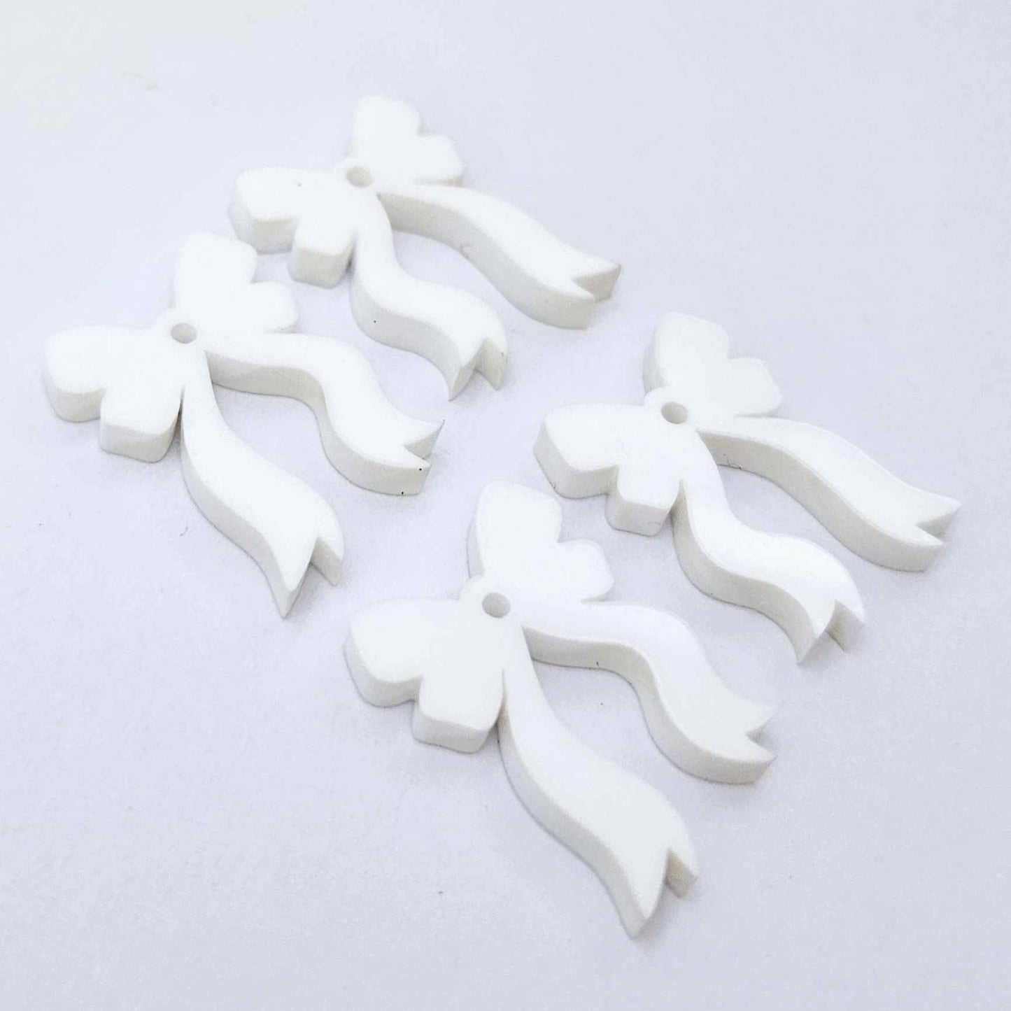 Two pairs of white acrylic bow dangle  earring blanks laying flat