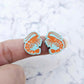 One pair of paint-filled pastel aqua acrylic prawn stud earring blanks shown on a finger for size reference