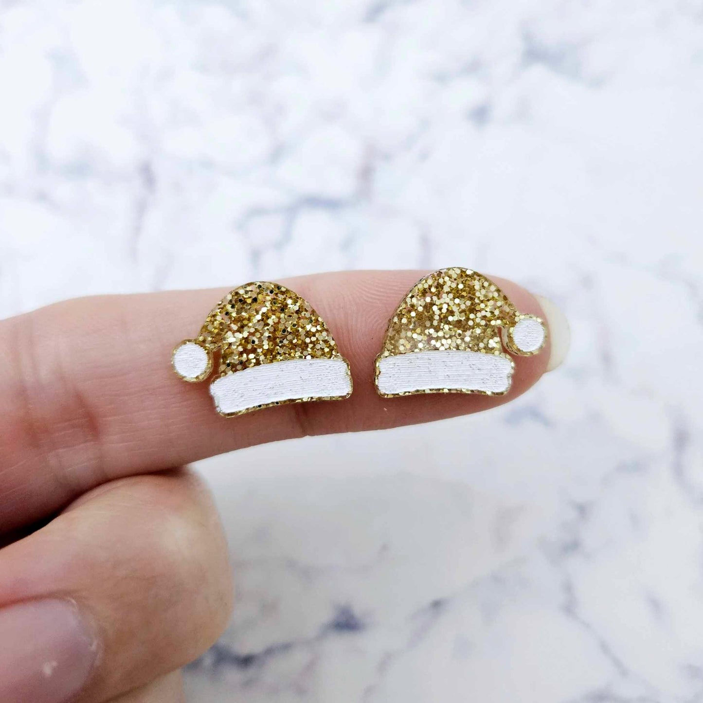 One pair of paint-filled gold glitter acrylic Santa hat stud blanks (no hole) shown on a finger for size reference