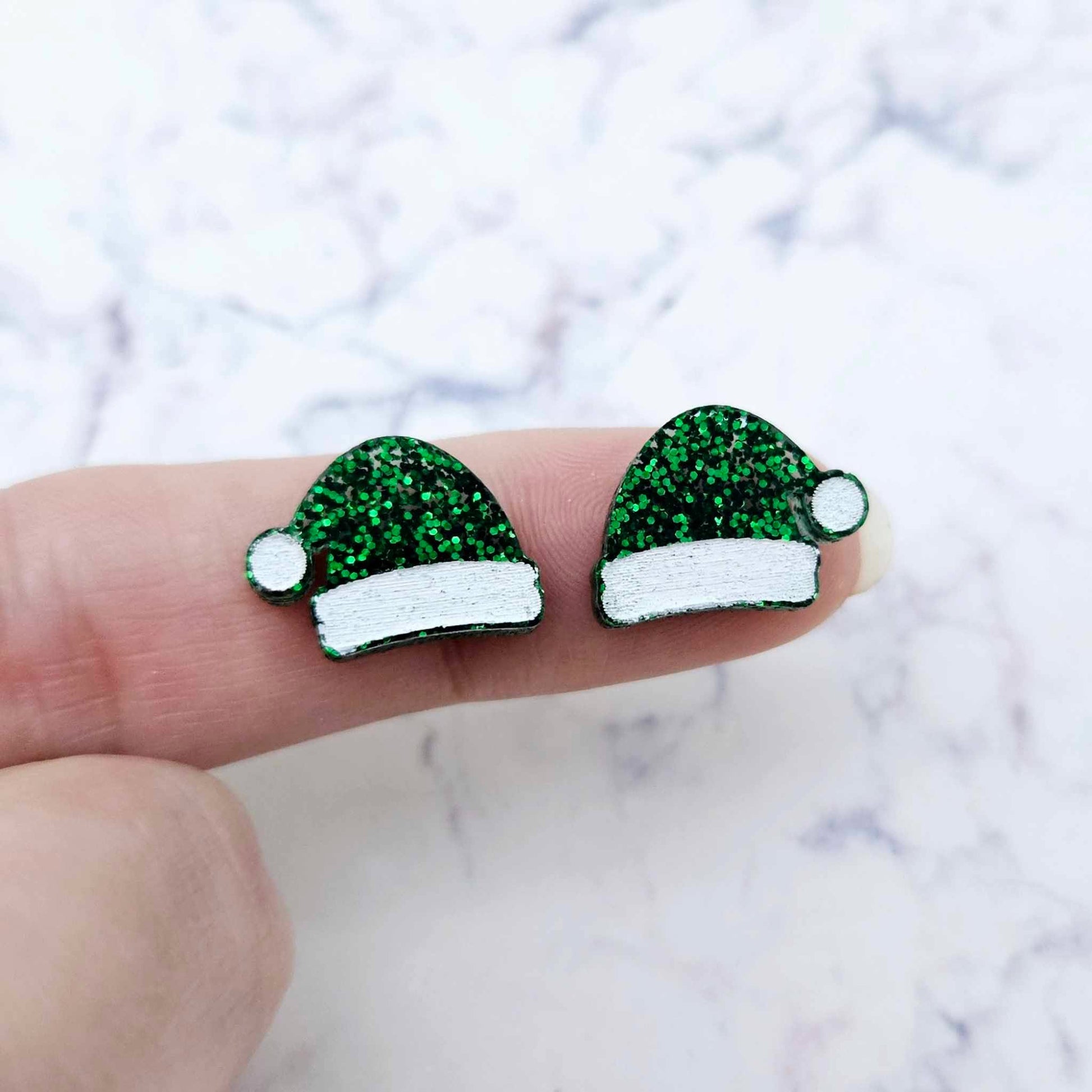 One pair of paint-filled green glitter acrylic Santa hat stud blanks (no hole) shown on a finger for size reference.