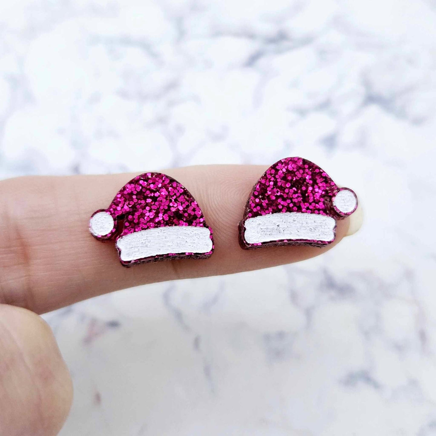 One pair of paint-filled hot pink glitter acrylic Santa hat stud blanks (no hole) shown on a finger for size reference