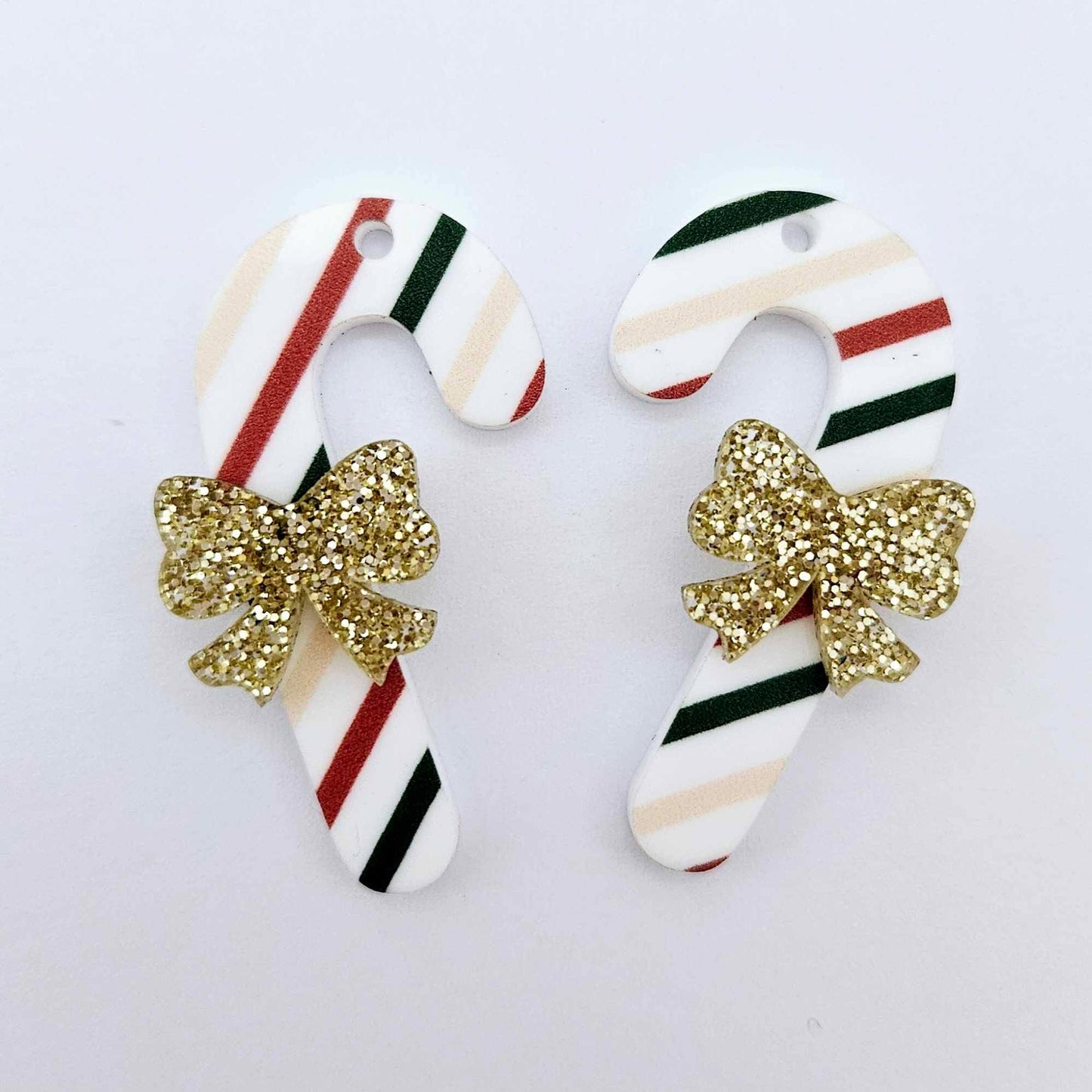 One pair of Stripy Christmas UV printed acrylic candy cane dangle earring blanks laying flat with gold glitter bows attached